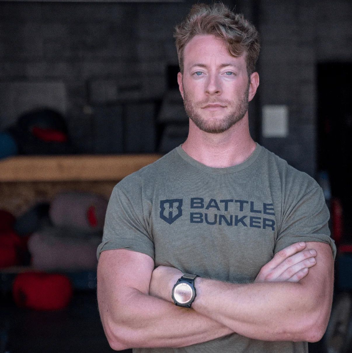 Man with crossed arms wearing a Battle Bunker T-shirt in a dimly lit room.